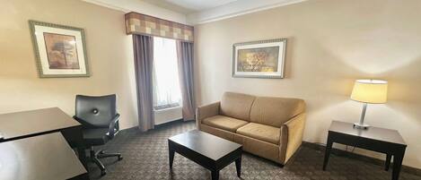 A hotel room with a sofa, a desk, a chair, a coffee table, and two lamps.