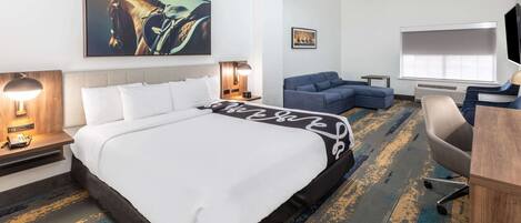 Una habitación de hotel con una cama grande, un escritorio, un sofá, un televisor y obras de arte en las paredes.