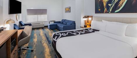 A hotel room with a bed, a desk, a chair, a sofa, a TV, and a painting on the wall.