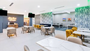 Un hall d’hôtel moderne comprenant un comptoir d’accueil, des espaces de détente et un espace repas.