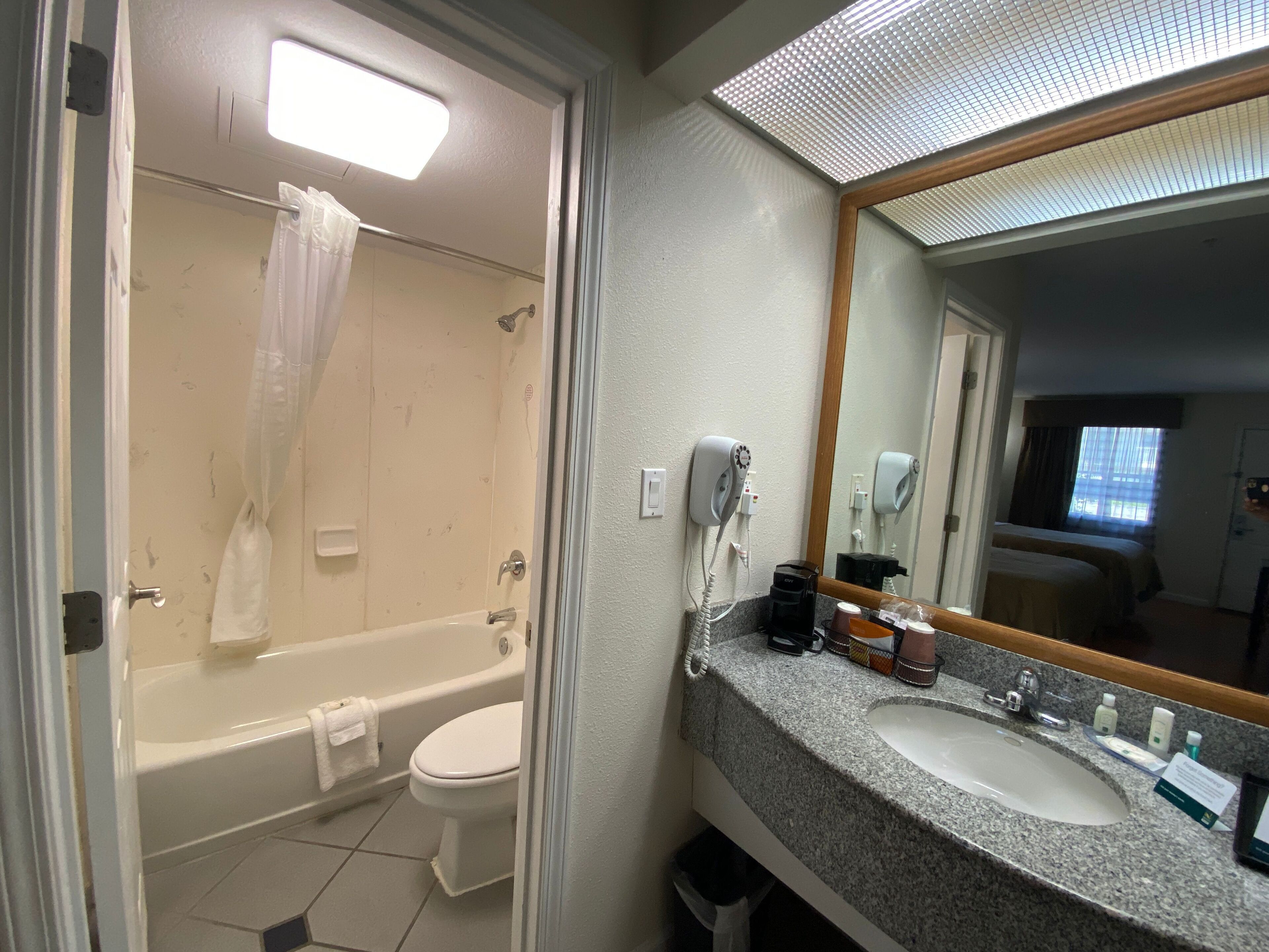 A bathroom with a bathtub, toilet, and sink. There is a shower curtain, a hairdryer, and a mirror.