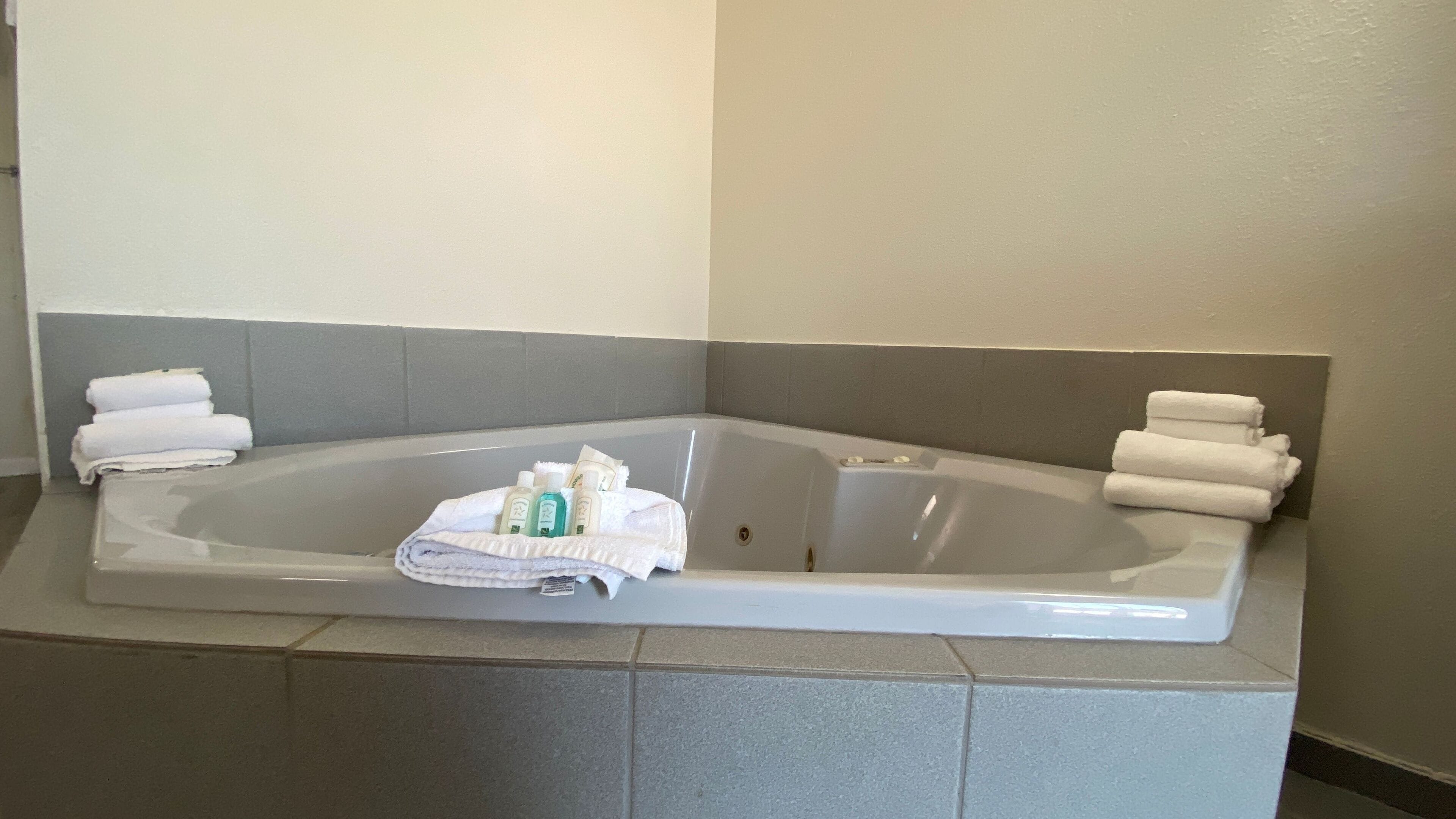 A corner bathtub with towels and toiletries.