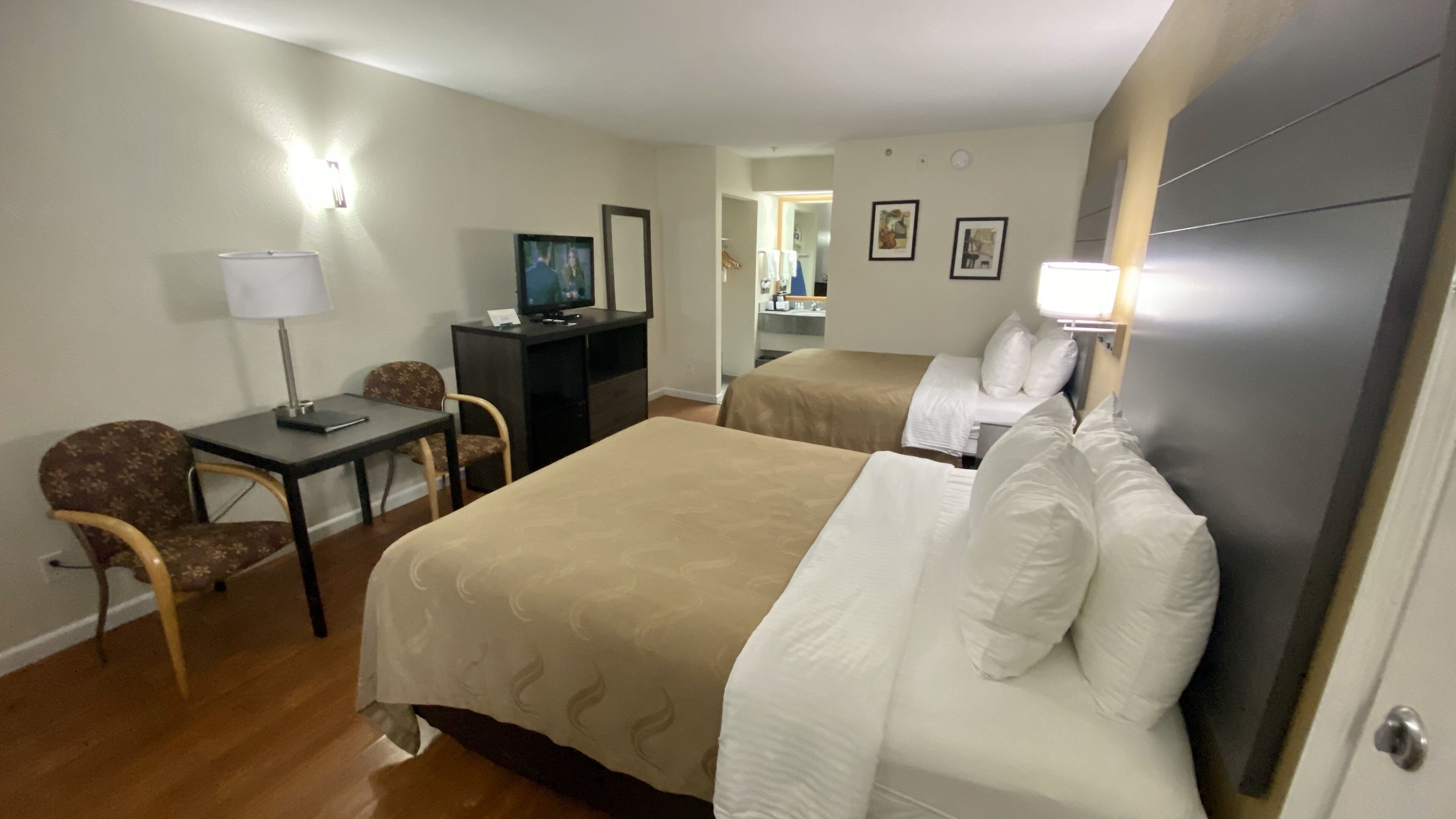 A hotel room with two beds, a desk, a chair, a TV, and a wardrobe.