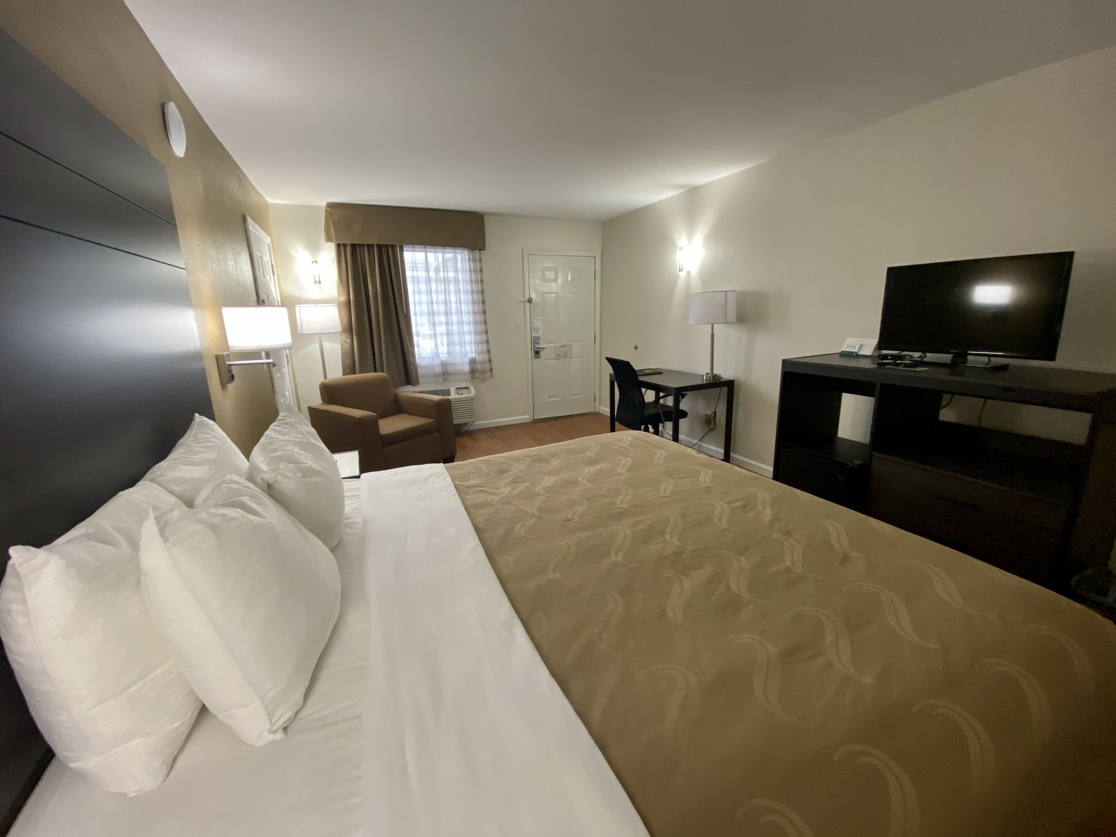 A hotel room with a large bed, a desk, a chair, a television, and a window with curtains.