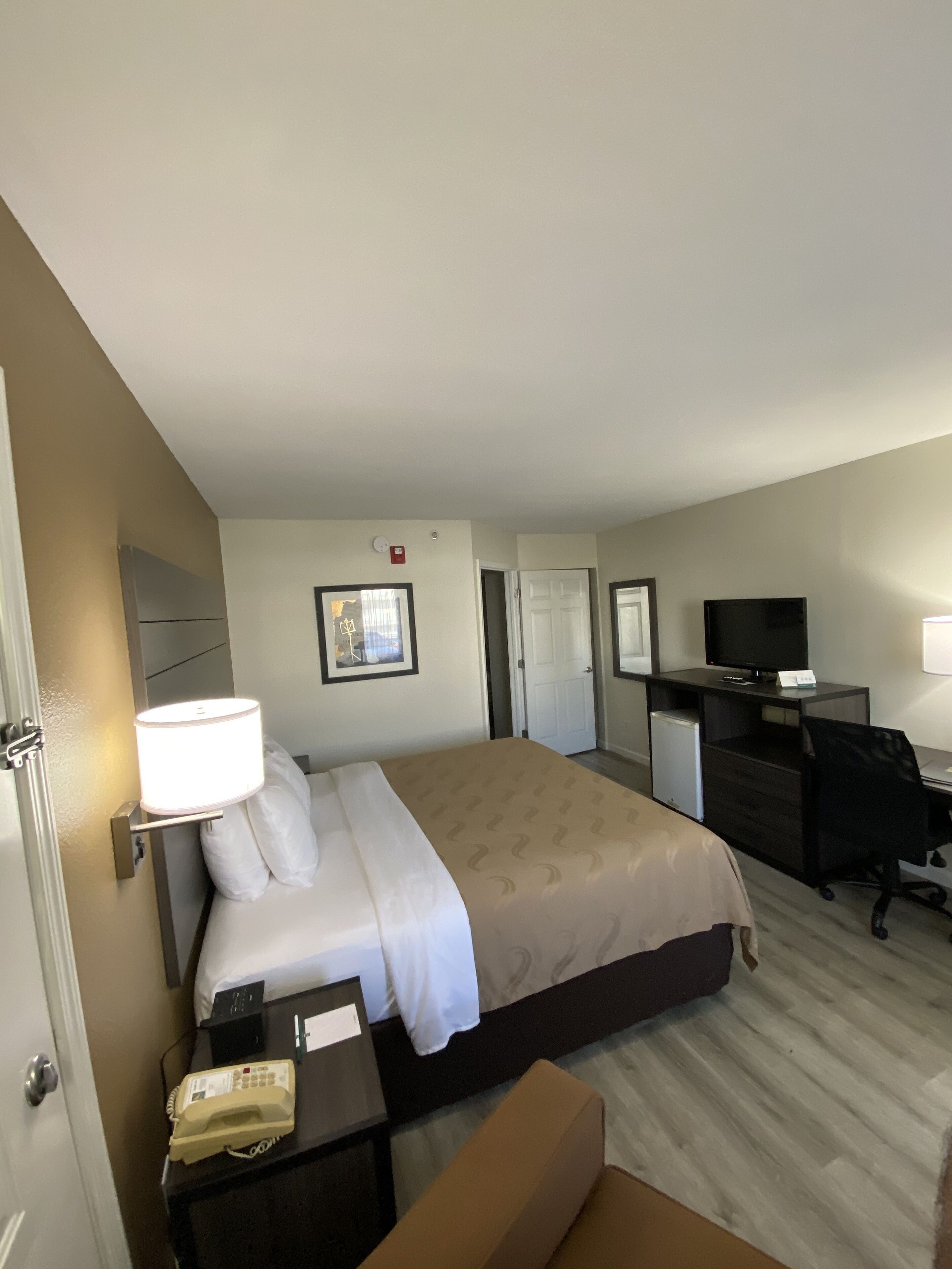 Habitación de hotel con una cama, un escritorio con computadora, televisor y teléfono.