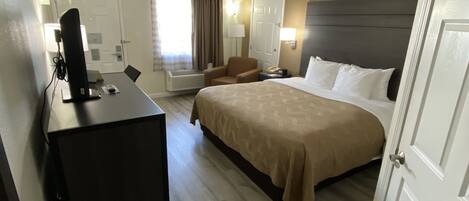 A hotel room with a bed, desk, chair, and a television.