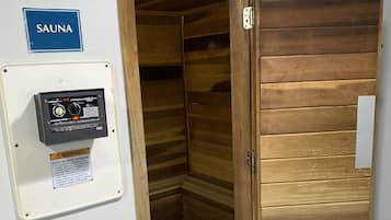 Un cuarto de sauna con paredes de madera y una puerta, un panel de control con un letrero de advertencia y un cartel que indica el propósito de la sala.