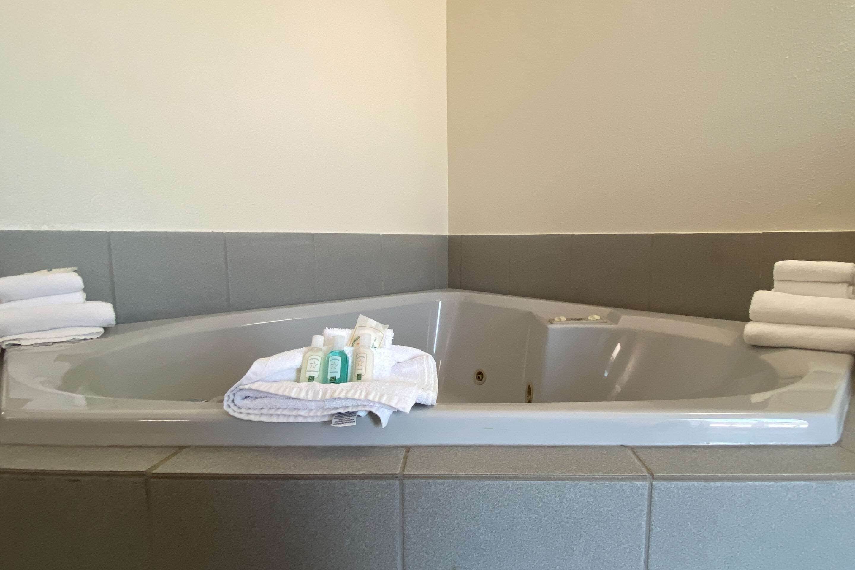 A corner bathtub with white towels and toiletries.