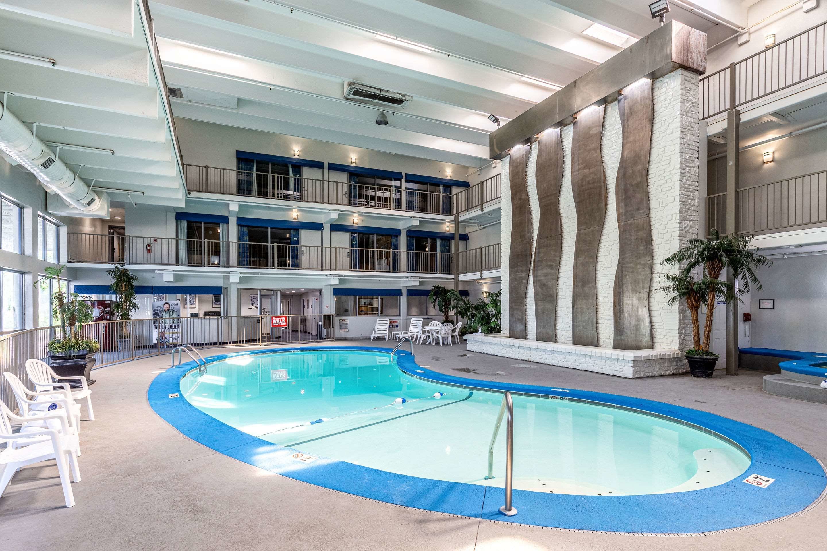 Une piscine intérieure avec un bord bleu, entourée de chaises blanches et de plantes en pot.