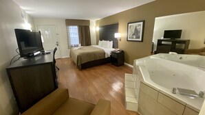 A hotel room with a bed, a desk with a computer, a TV, a large bathtub, and a chair. - Quality Inn Branson - Hwy 76 Central (Branson)
