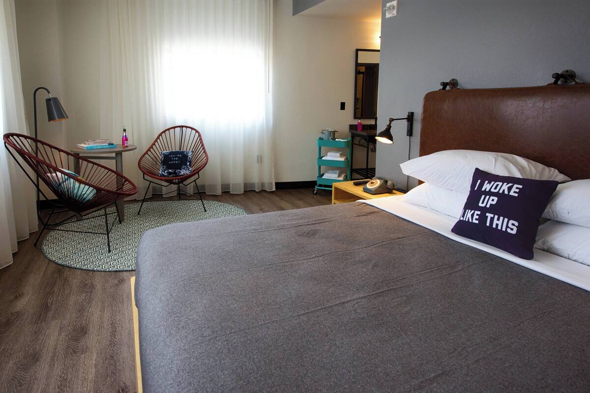 A hotel room with a large bed, a chair, a small table, and a nightstand.