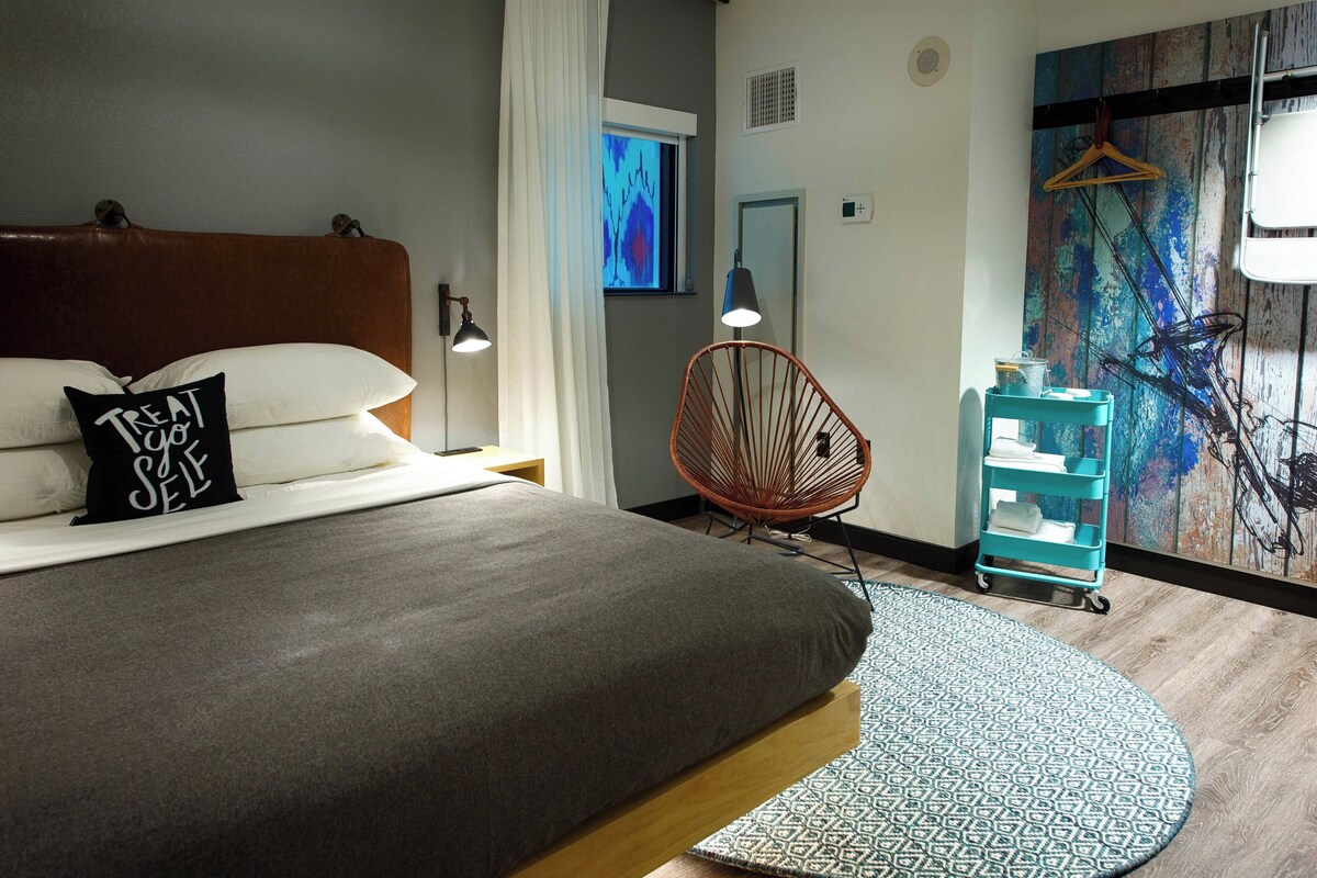 A modern bedroom with a large bed, a hanging chair, a small table, and a wall-mounted TV.