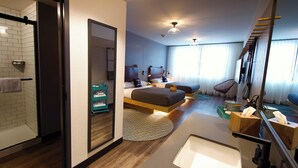 A modern hotel room with a shower, a large mirror, a bed with two pillows, a bedside table, a chair, and a window with curtains.