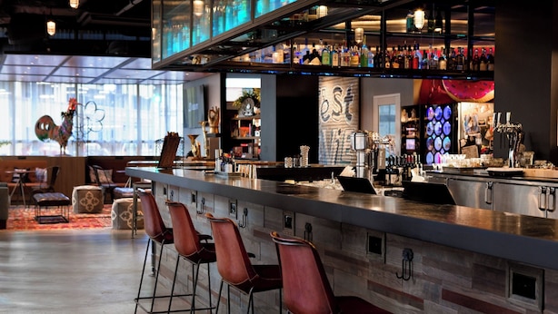 A modern bar area with a long counter, multiple stools, and a variety of bottles and glasses.