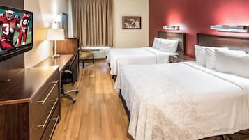 Habitación de hotel con televisión, escritorio, silla, dos camas y ventana con cortinas.