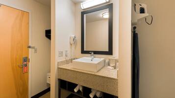 Une salle de bain avec un lavabo blanc, un miroir, un porte-serviettes et une porte sur laquelle est apposée une pancarte indiquant de ne pas déranger.