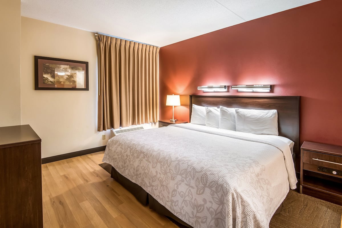 A hotel room with a large bed, a nightstand, a lamp, a framed picture on the wall, and a window with curtains.