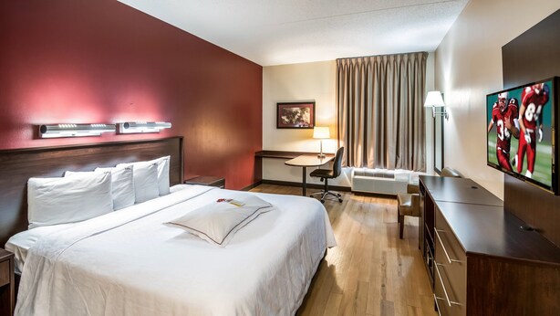 A hotel room with a large bed, a desk, a chair, a TV, and a lamp.