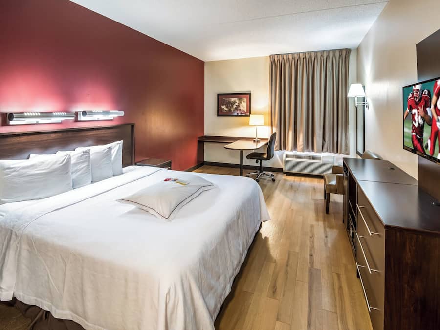 A hotel room with a large bed, bedside tables, a desk, a chair, a TV, and a window with curtains.
