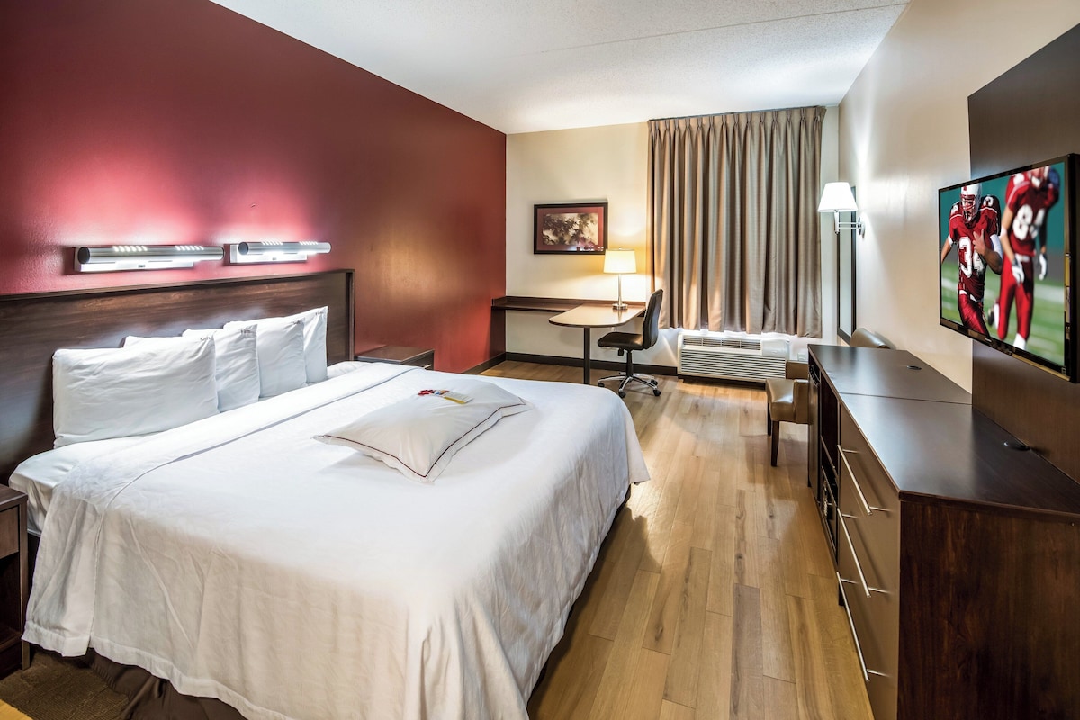 A hotel room with a large bed, a desk, a chair, a TV, and a window with curtains.