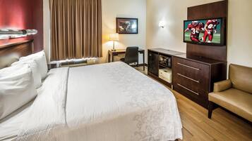 A hotel room with a bed, a desk, a television, and a seating area.