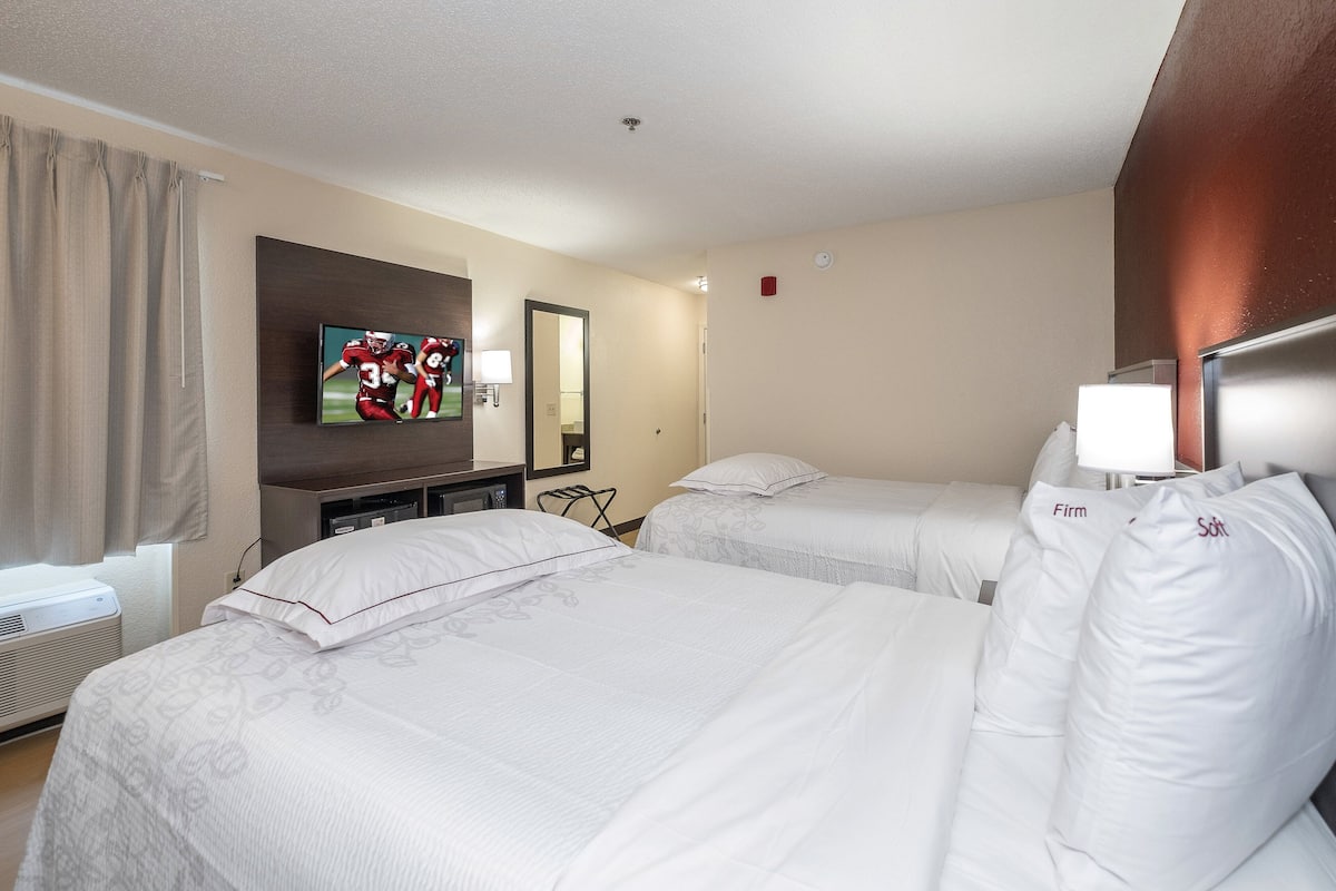 A hotel room with two beds, a TV, a mirror, and a desk with a lamp.
