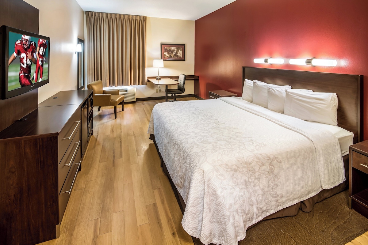 A hotel room with a bed, a desk, a chair, a television, and a lamp.