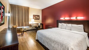 Una habitación de hotel con cama, escritorio, silla y un cuadro en la pared.