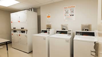A laundry facility with multiple washing machines and dryers, a poster on the wall, and a table.