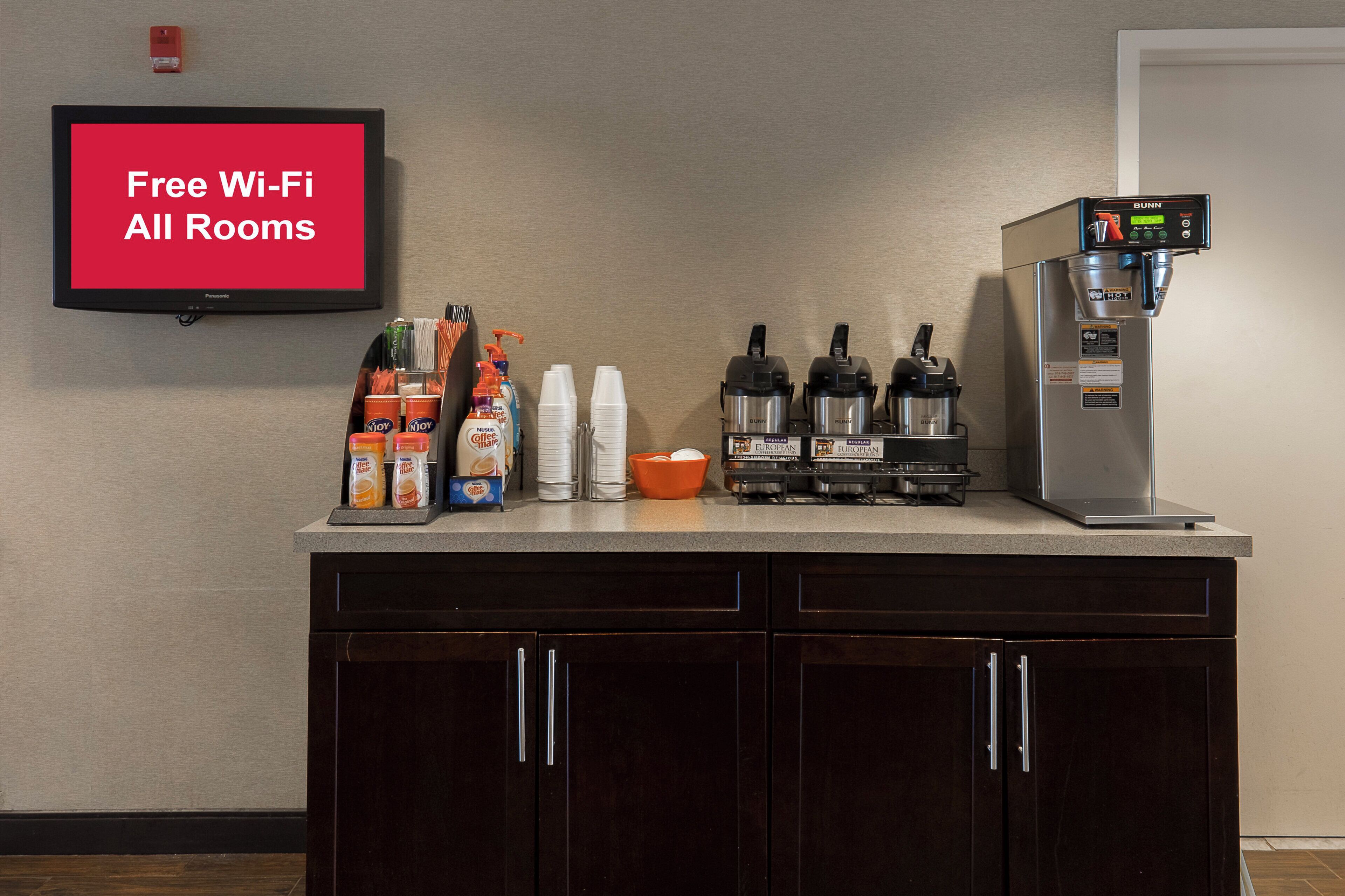A kitchenette with a coffee machine, coffee pods, and a TV displaying 'Free Wi-Fi All Rooms'.