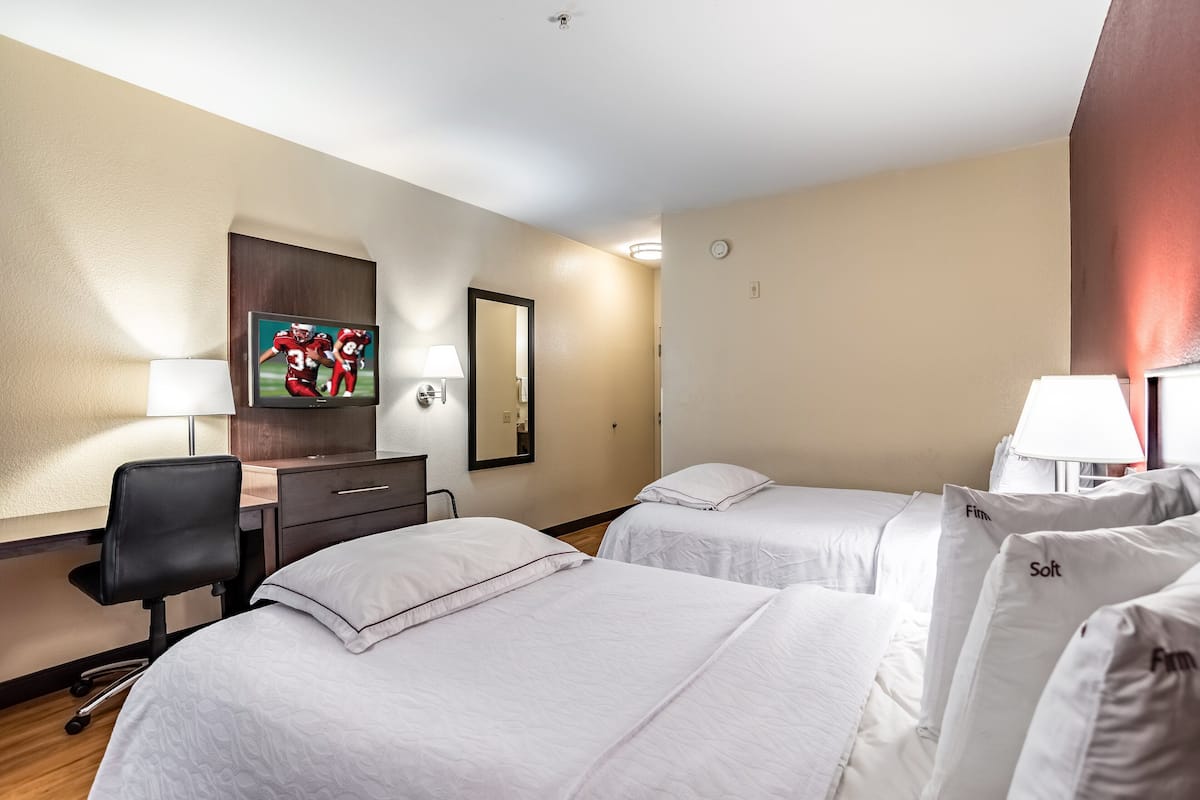 Ett hotellrum med två sängar, ett skrivbord, en stol, en TV och en spegel.