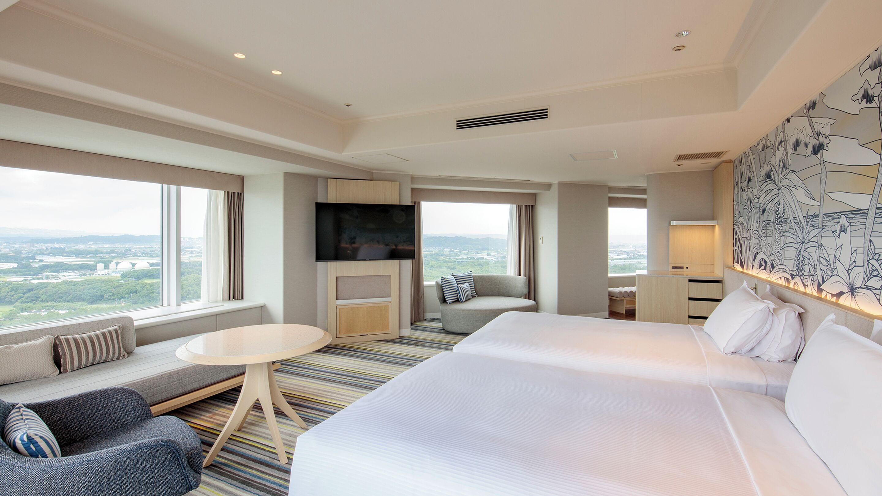 Habitación de hotel con una cama grande, un sofá, una mesita, un televisor y vistas a la ciudad.