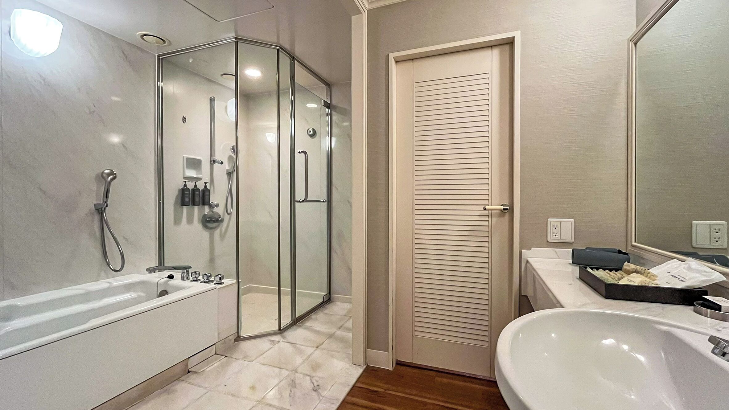 A modern bathroom with a glass-enclosed shower, a white bathtub, and a sink with a mirror.