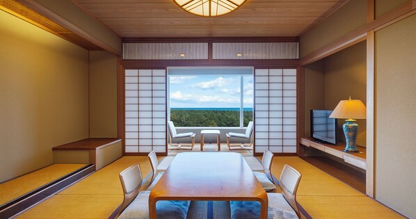 A room with a wooden table, chairs, a TV, and a view of the ocean. - Phoenix Seagaia Ocean Tower (Miyazaki)