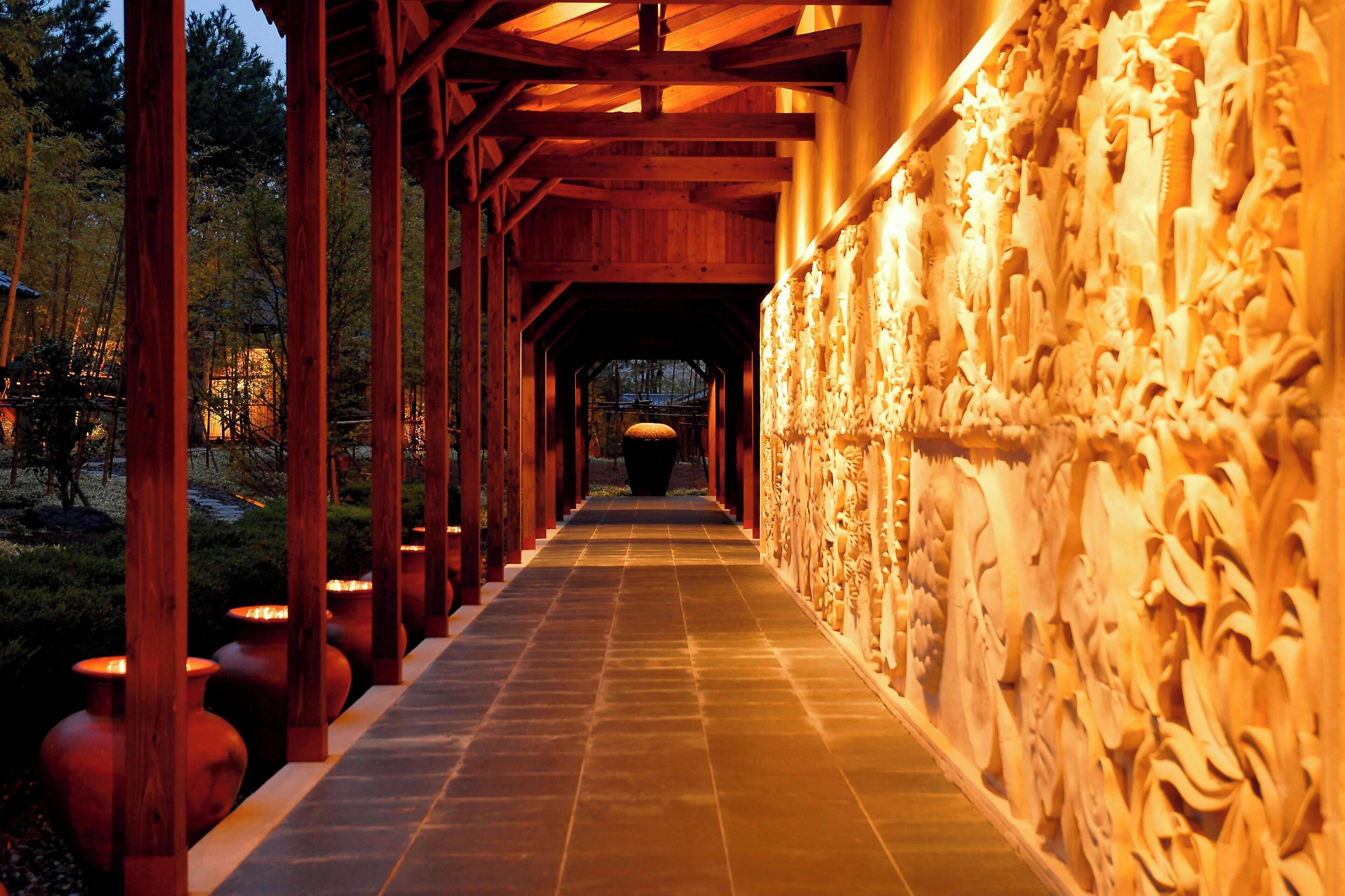 A corridor with wooden beams and a tiled floor, leading to a darkened area at the end.