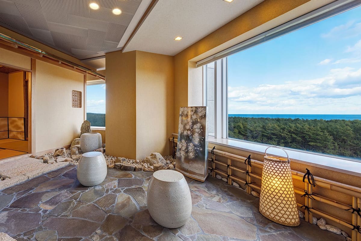 A spa room with stone flooring, a large window with a forest view, and a traditional Japanese sliding door.