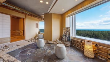 Un cuarto de spa con suelo de piedra, un ventanal con vista al bosque y una puerta corredera tradicional japonesa.