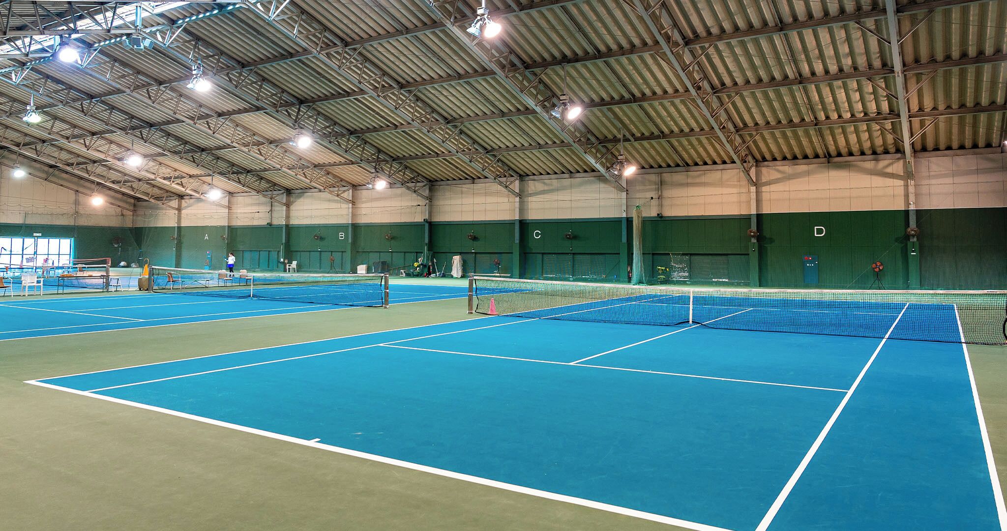 An indoor tennis court with multiple courts, a high ceiling, and green walls.