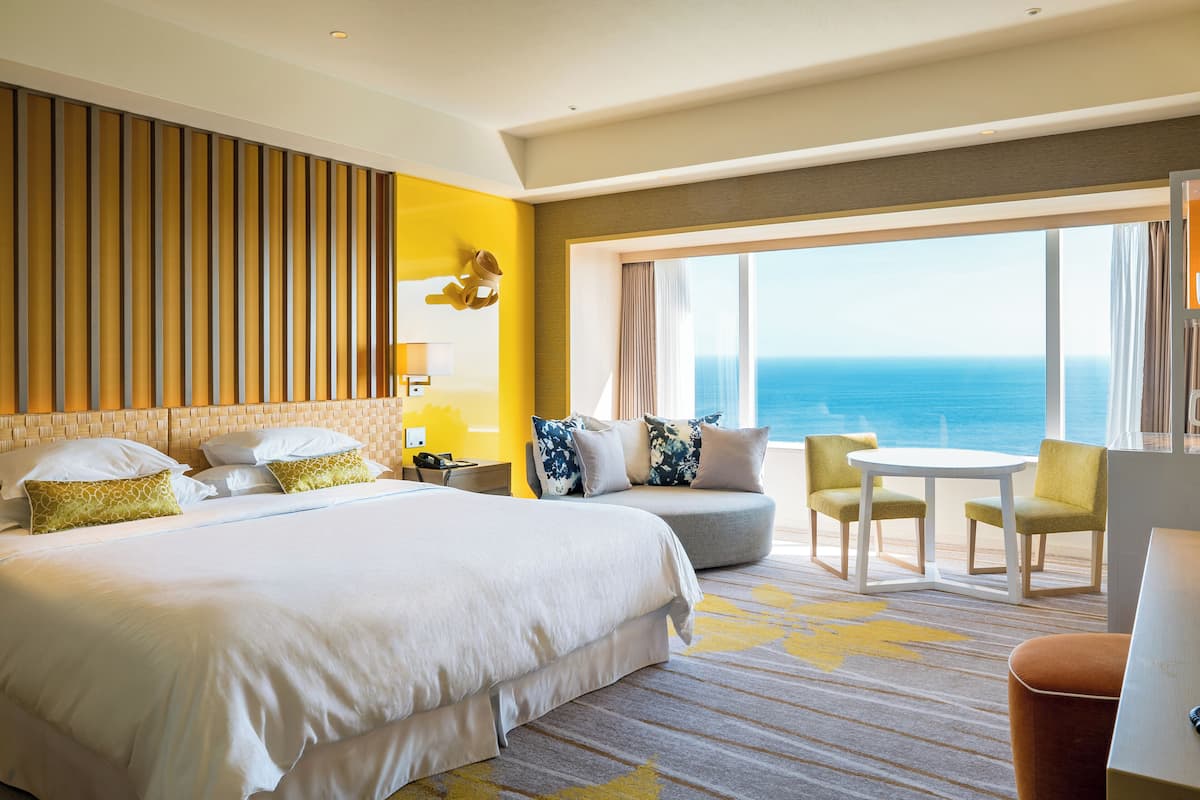 A hotel room with a large bed, a sofa, a small table, and a view of the ocean.
