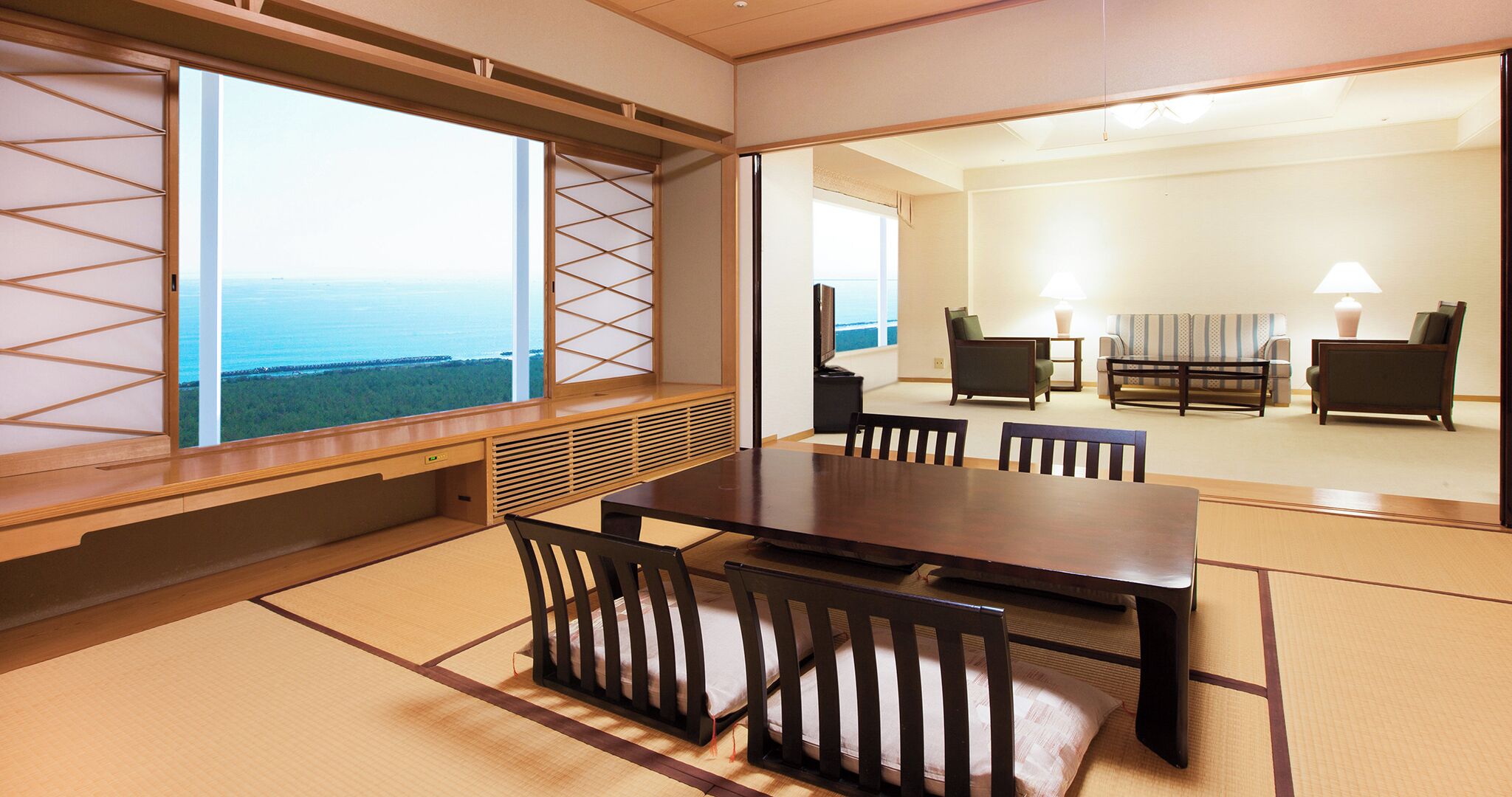 Een traditionele Japanse kamer met tatami vloeren, een lage tafel met stoelen en uitzicht op de zee door een shoji scherm.