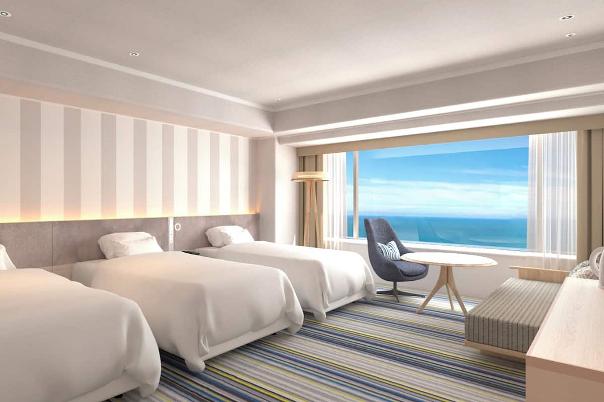A hotel room with two beds, a small round table, a chair, a TV, and a large window with a view.
