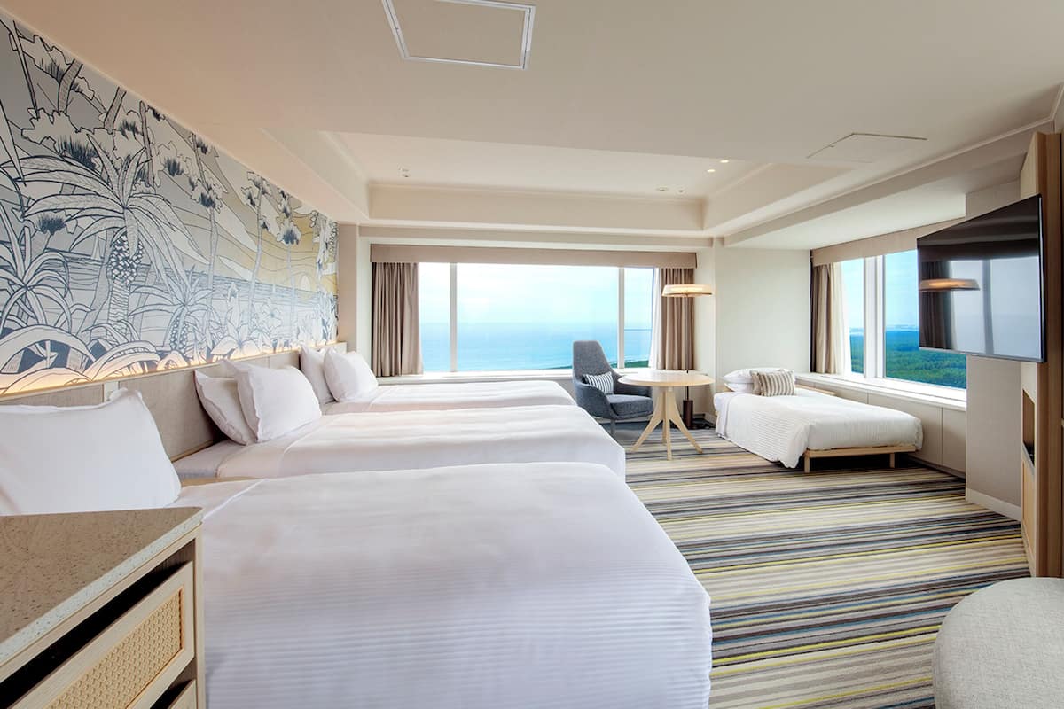 A hotel room with two beds, a seating area, a large window with a view, and a wall mural.