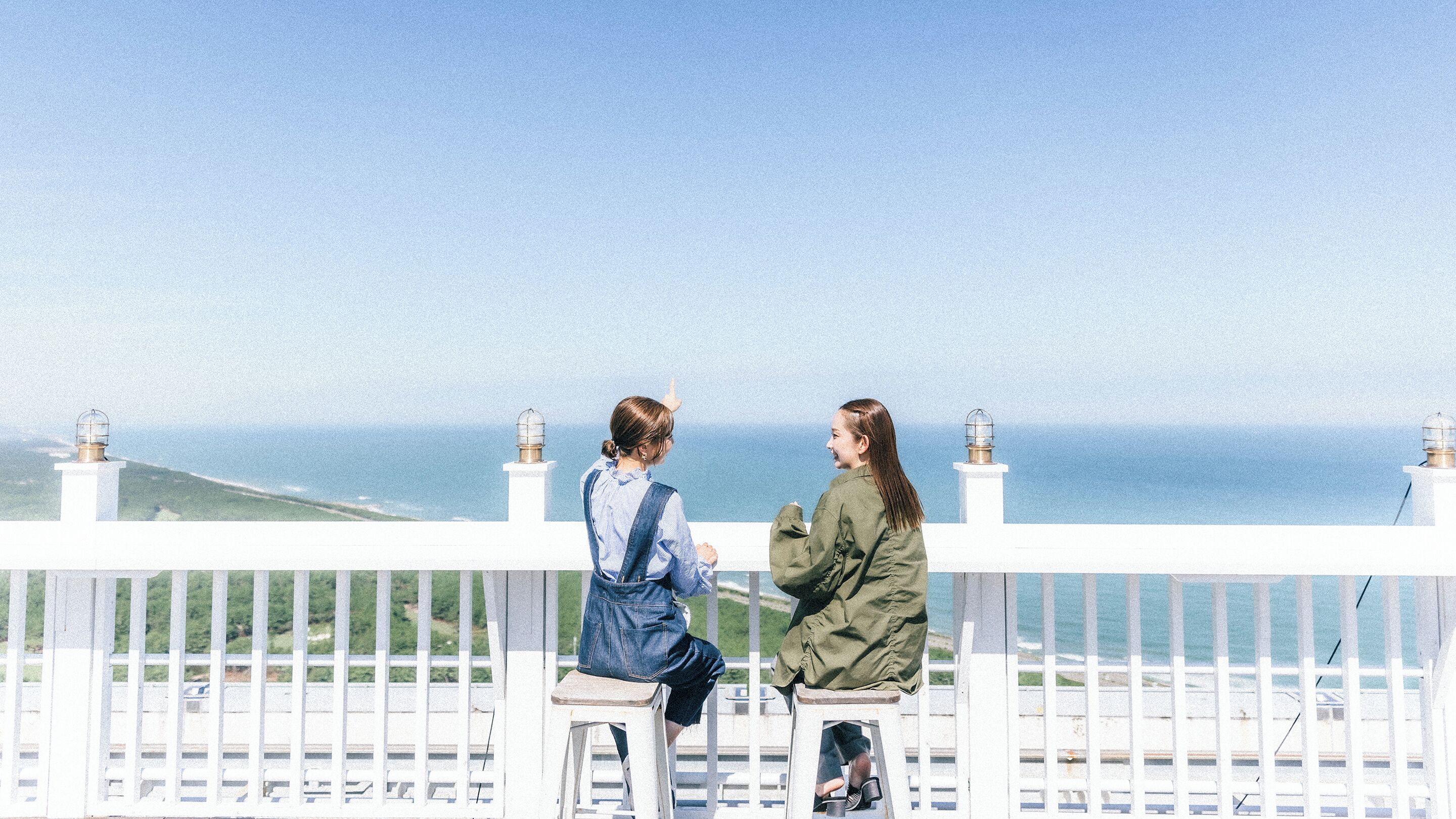 Two people sitting on a white balcony with a view of the ocean.