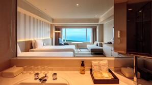 A hotel room with two beds, a sofa, a small table, a TV, and a bathroom with a sink and toiletries. - Phoenix Seagaia Ocean Tower (Miyazaki)