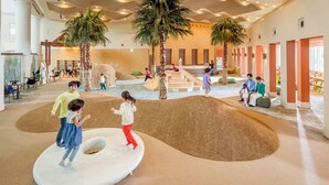 A children's play area with soft play structures, palm trees, and a seating area for adults. - Phoenix Seagaia Ocean Tower (Miyazaki)