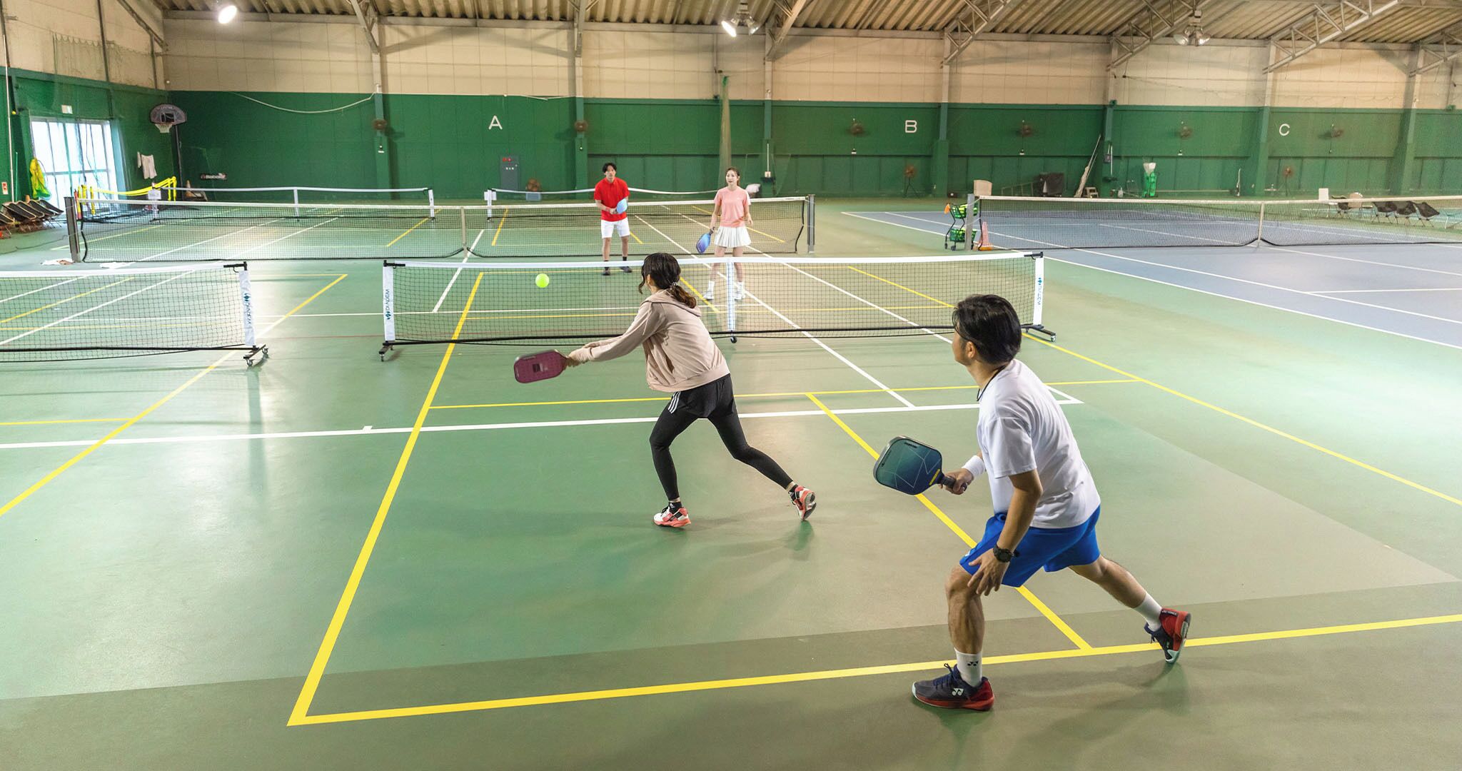 Una cancha de tenis cubierta con varias canchas, paredes verdes y un techo alto.