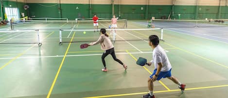 Una cancha de tenis cubierta con varias canchas, paredes verdes y un techo alto.