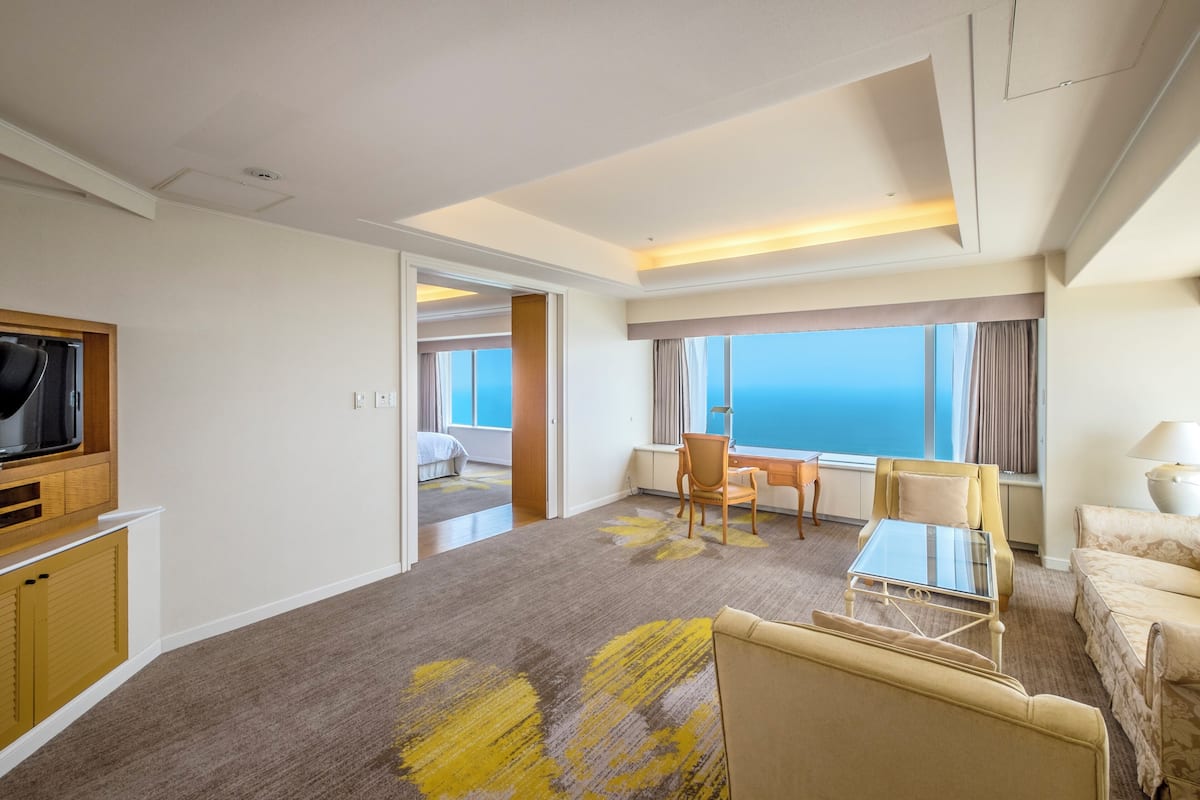 A hotel room with a large bed, a desk, a chair, a TV, and a view of the ocean.