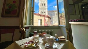 A dining area with a table set for breakfast, a window with a view of a tower, and a painting on the wall. - Hotel De Lanzi (Florence)
