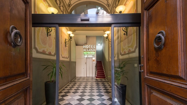 Entrada de hotel con suelo a cuadros, puertas de madera y una escalera que sube al nivel superior.